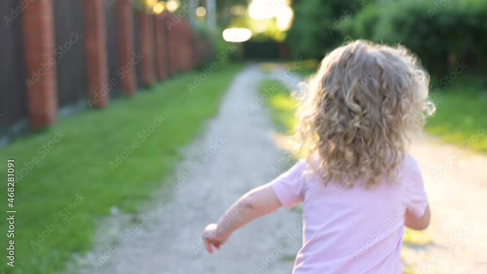 A little curly-haired girl runs forward along the village path. Hair curls and is brightly lit by sunlight. Slow motion of running child A little curly-haired girl runs forward along the village path. Hair curls and is brightly lit by sunlight. Slow motion of running child