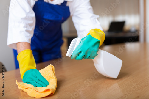 Image of gloved woman's hands cleaning an office desk with a rag and detergents. Close-up image