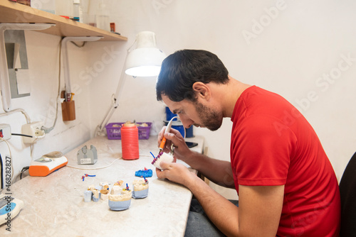 A man works at a dental technician's desk in a workshop doing electric soldering