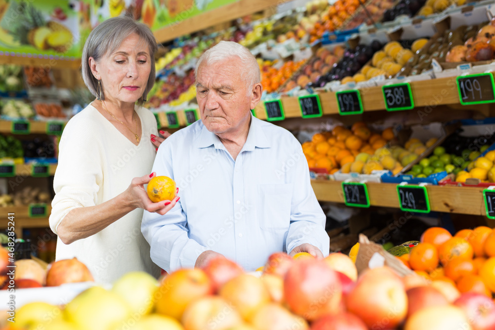 Elderly married couple choosing different fruits together in vegetable supermarket