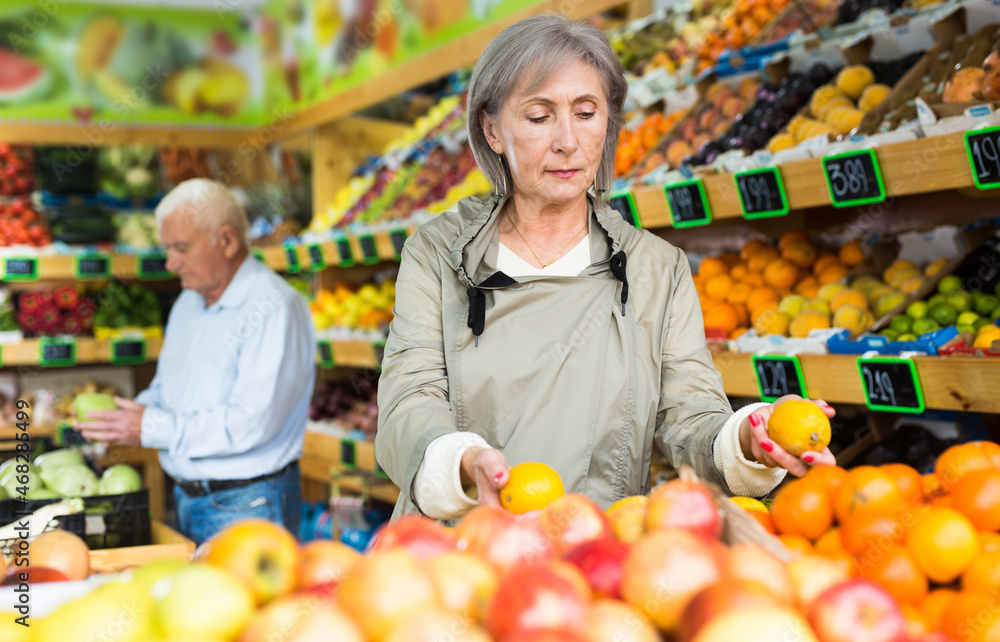 Positive female buyer shopping in supermarket, choosing ripe apples in fruit and vegetable department
