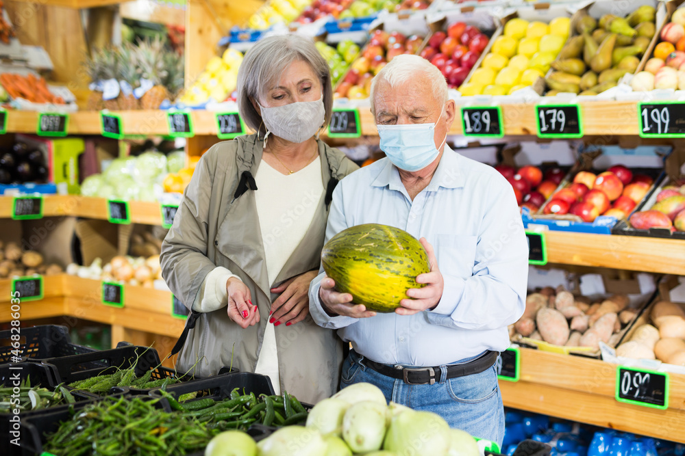 Married couple in protective mask buy ripe watermelon in the supermarket