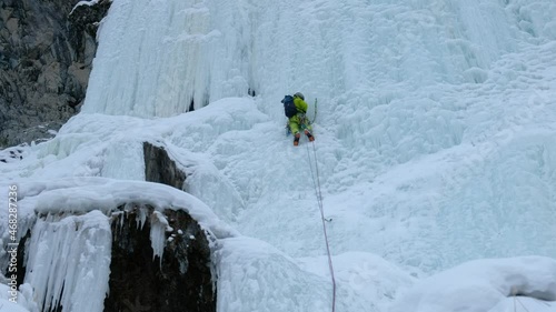 Alpinist man with ice tools axe climbing a frozen waterfall, a large wall of ice