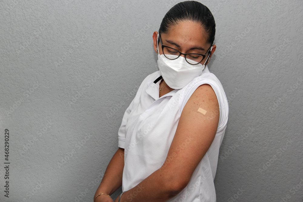 Latin young adult woman with glasses shows her arm recently vaccinated against covid-19 in the new normal for the coronavirus pandemic
