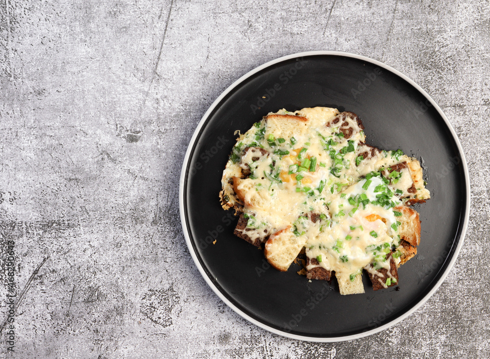 Fried eggs with bread, cheese and green onions on a round plate on a dark background. Top view, flat lay Fried eggs with bread, cheese and green onions on a round plate on a dark background. Top view, flat lay