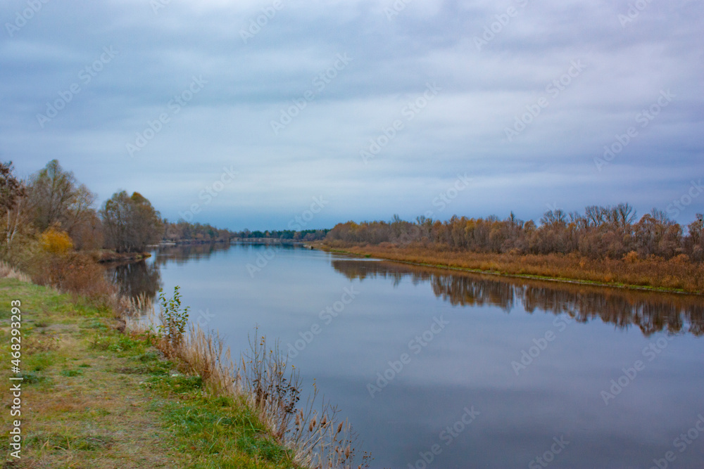 Two banks of the same river on a cloudy day. Autumn landscape of the river and yellowed forest.
