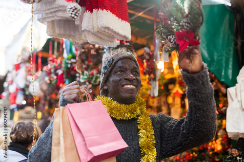 Cheerful African American looking for New Year decorations in traditional street market.