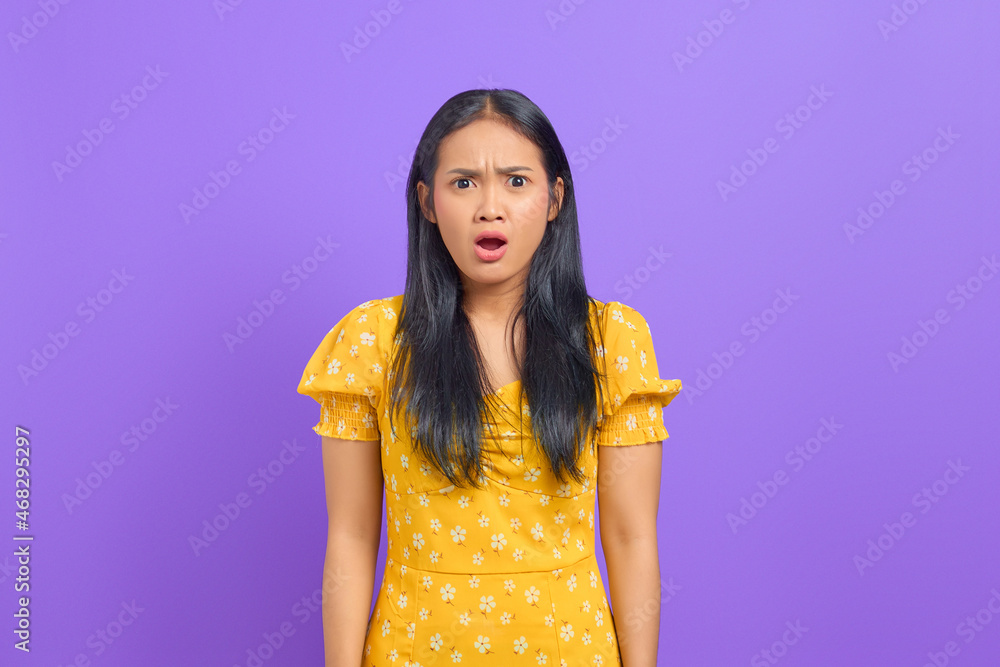 Portrait of shocked young Asian woman wearing a yellow dress on purple background Portrait of shocked young Asian woman wearing a yellow dress on purple background