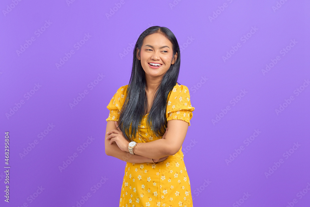 Smiling young Asian woman with crossed arms and looking away on purple background Smiling young Asian woman with crossed arms and looking away on purple background