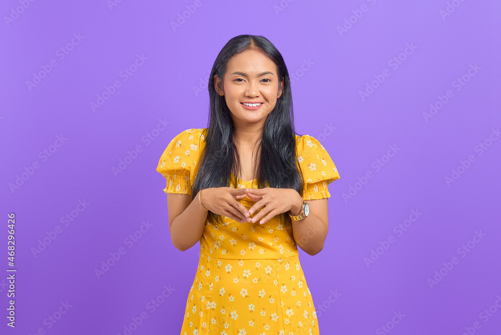 Smiling young Asian woman keeps hand together and feels optimistic on purple background Smiling young Asian woman keeps hand together and feels optimistic on purple background