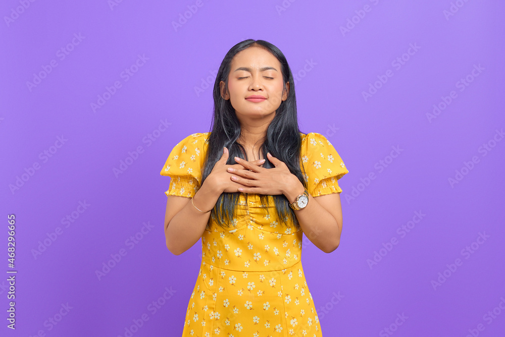 Beautiful young Asian woman put hands on chest on purple background Beautiful young Asian woman put hands on chest on purple background