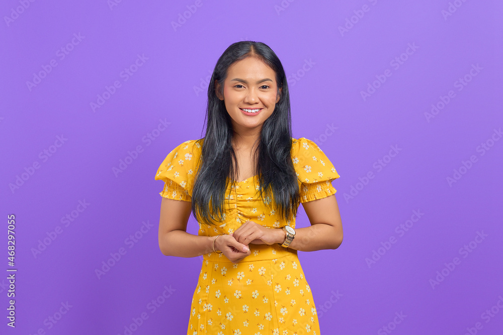 Smiling young Asian woman keeps hand together and feels optimistic on purple background Smiling young Asian woman keeps hand together and feels optimistic on purple background