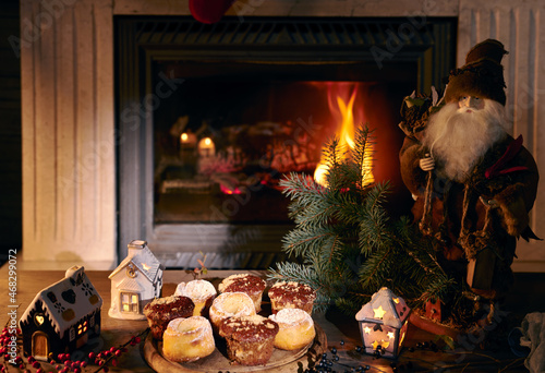 Santa Claus, a dish with muffins, a branch of a Christmas tree, berries with a burning fireplace in the background