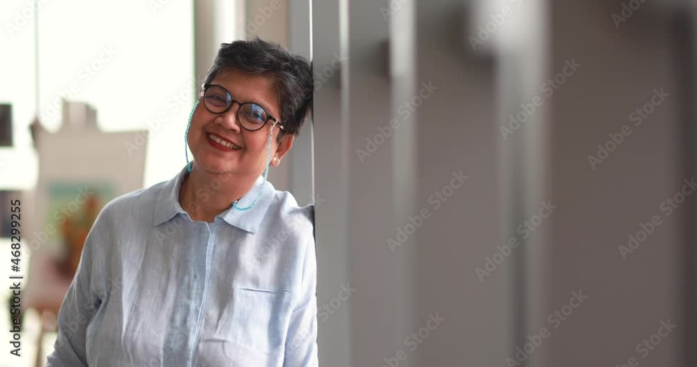 Positive mature Asian female smiling for camera at home Positive mature Asian female smiling for camera at home