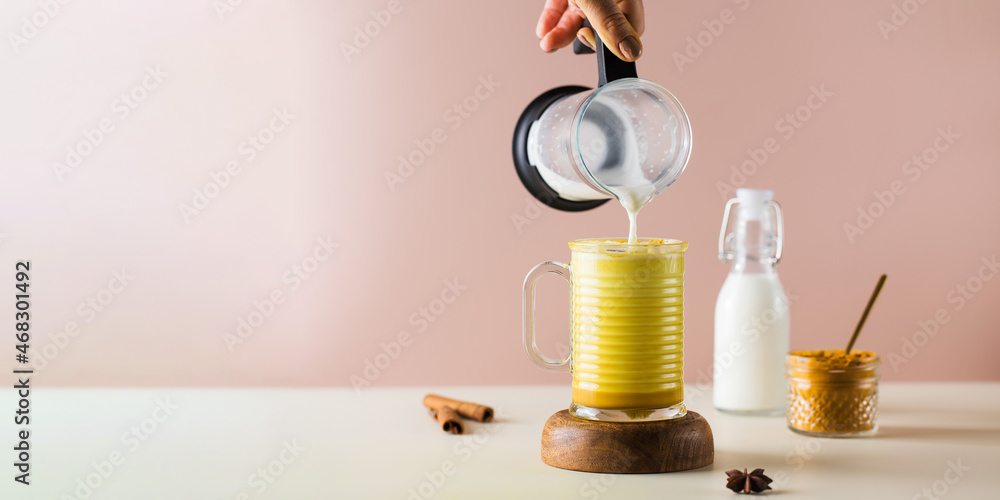 Banner milk froth is poured into a glass with golden latte with turmeric. Moon milk for better sleep. 