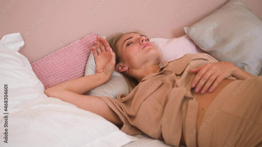 Sleepy dressed blonde woman wakes up on bed and covers head with soft white pillow avoiding bright daylight and noise at home slow motion Sleepy dressed blonde woman wakes up on bed and covers head with soft white pillow avoiding bright daylight and noise at home slow motion