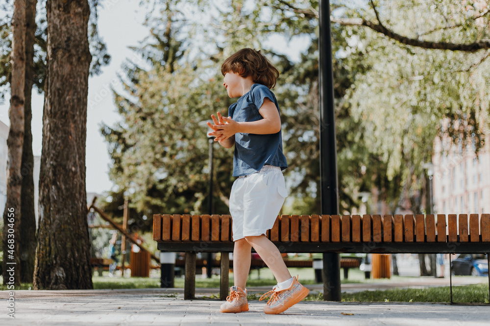 little brunette boy in a blue T-shirt and white shorts runs along a paved path in the city square. healthy active child walks outdoors. lifestyle. space for text. High quality photo little brunette boy in a blue T-shirt and white shorts runs along a paved path in the city square. healthy active child walks outdoors. lifestyle. space for text. High quality photo