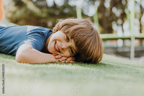 portrait of a little boy in a blue T-shirt lying on the green grass. child is playing in the park. outdoor activities, lifestyle. space for text. High quality photo