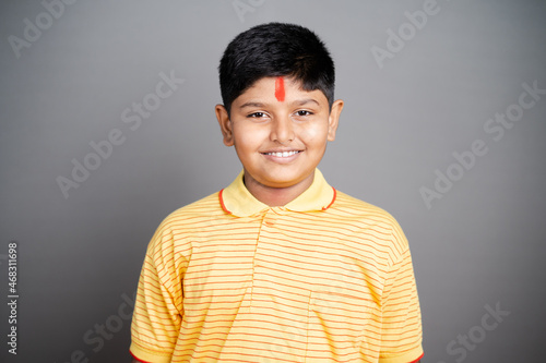 Happy Hindu kid with kumkum Bindi or Tilak on forehead by looking at camera on studio background - concept of smiling and positive joyful expression photo