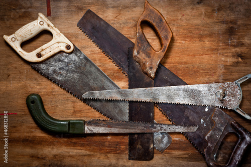 Old vintage metal saws for wood of different shapes and sizes, crumpled on a wooden background. photo