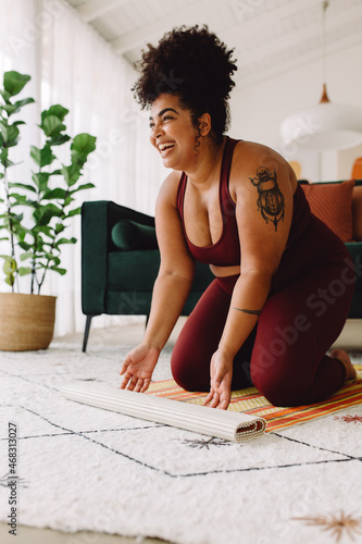 Happy fitness woman unfolding yoga mat at home