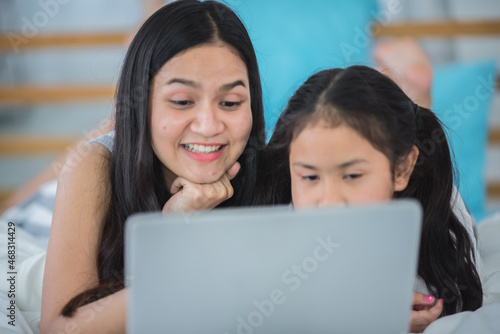children and girl sisters having fun to watching online video on laptop computer cyberspace, childhood people family or young mother and little daughter are happy together at home with technology