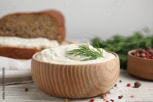 Tasty creamy dill sauce in bowl on white wooden table, closeup