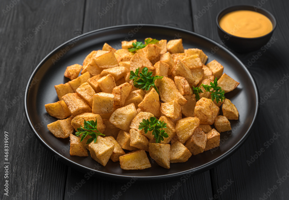 Patatas bravas with sauce and fresh parsley on a black background.