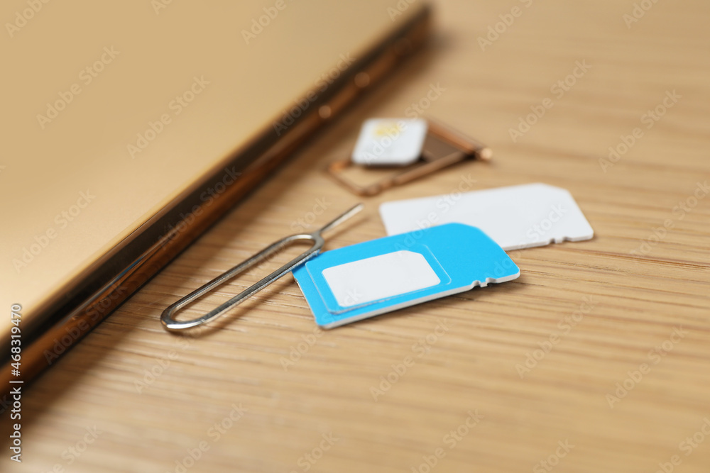 SIM cards, mobile phone and ejector tool on wooden table, closeup SIM cards, mobile phone and ejector tool on wooden table, closeup