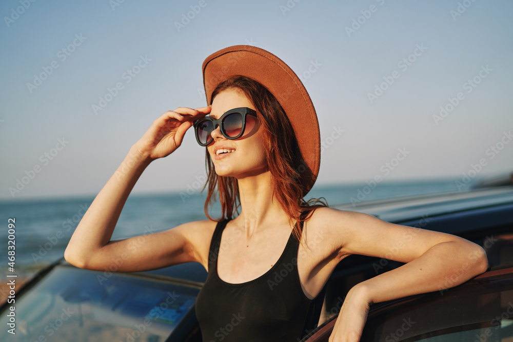 cheerful woman in sunglasses and a hat on the ocean near the car cheerful woman in sunglasses and a hat on the ocean near the car