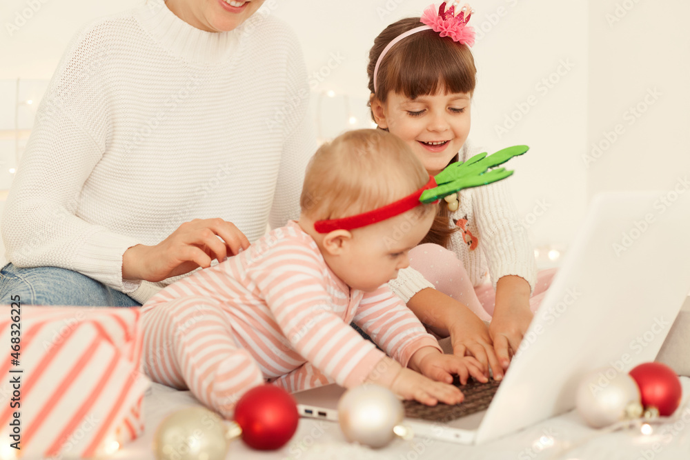 Happy positive girls posing with mother on bed during New year eve in front of laptop computer, spending time together, watching Christmas cartoons in evening. Happy positive girls posing with mother on bed during New year eve in front of laptop computer, spending time together, watching Christmas cartoons in evening.
