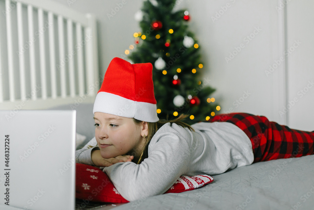 Caucasian girl in santa hat looking at laptop, watching movie. Concept of home christmas lifestyle. Caucasian girl in santa hat looking at laptop, watching movie. Concept of home christmas lifestyle.