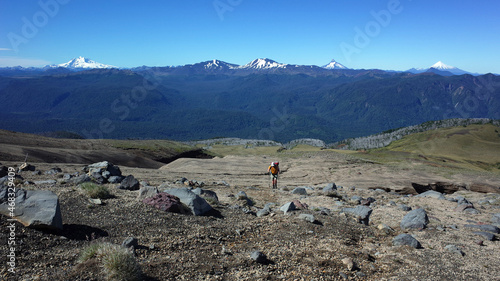 Man solo hiking up mountainside volcano Puyehue, Puyehue National Park, Chile, Patagonia. Volcanoes Tronador, Antillanca, Casablanca, Puntiagudo, Osorno of Andes Southern Volcanic Zone on horizon photo