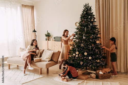 The concept of Christmas. A happy family with three children are preparing for the New Year holiday together decorating a Christmas tree in the cozy interior of the living room of the house in winter.