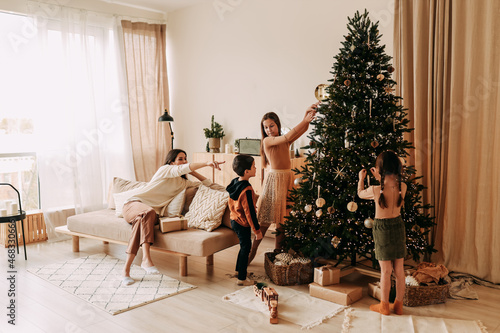 The concept of Christmas. A happy family with three children are preparing for the New Year holiday together decorating a Christmas tree in the cozy interior of the living room of the house in winter.