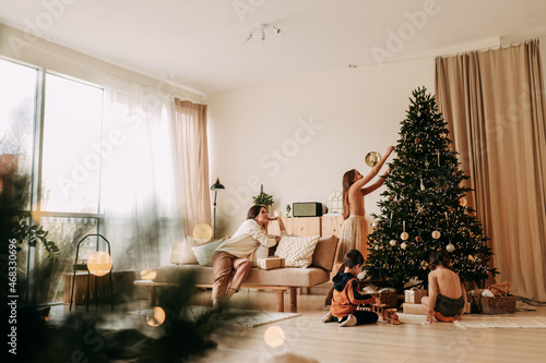 The concept of Christmas. A happy family with three children are preparing for the New Year holiday together decorating a Christmas tree in the cozy interior of the living room of the house in winter.