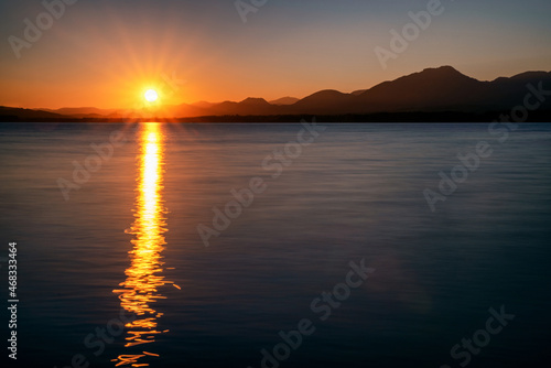 Reflecton of sunrays on water surface. Sun and silhouette of mountains at background