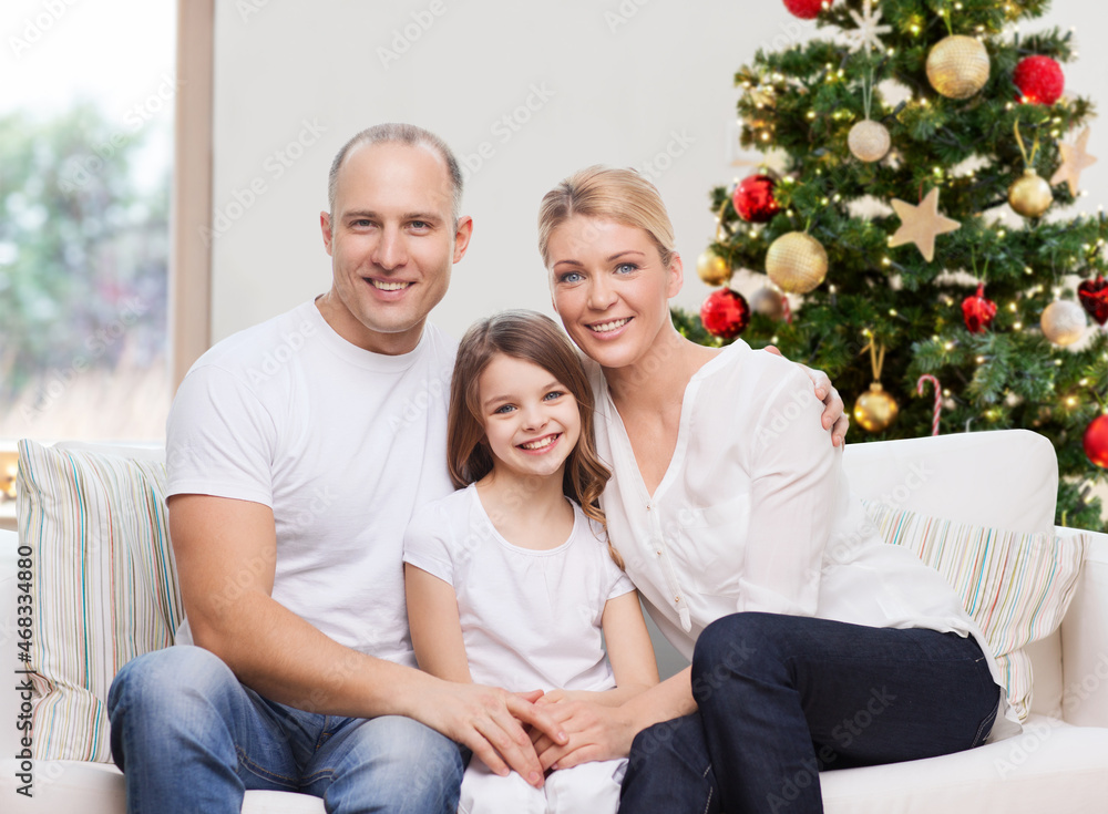 family, winter holidays and technology concept - portrait of happy mother, father and daughter sitting on sofa at home over christmas tree lights background family, winter holidays and technology concept - portrait of happy mother, father and daughter sitting on sofa at home over christmas tree lights background