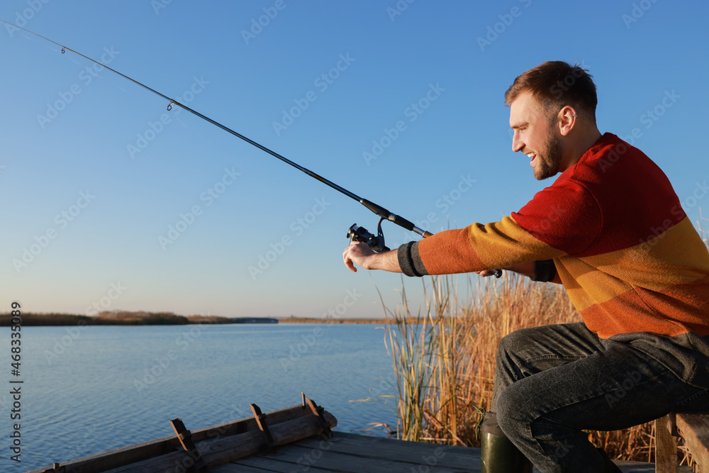 Fisherman with fishing rod at riverside on sunny day