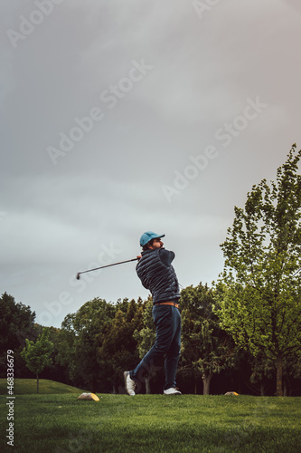 Man playing golf making an exit swing on a green field on a cloudy day