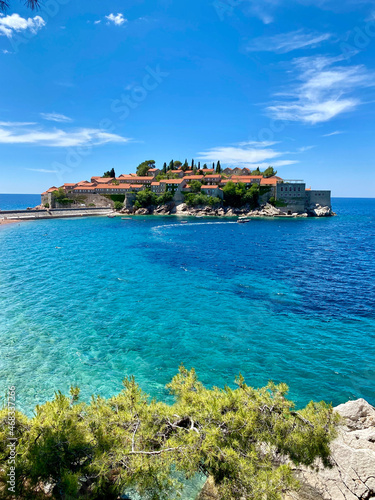 The village of Sveti Stefan, Montenegro, with red tiles on the roofs of houses, the sea with emerald water and dark blue water