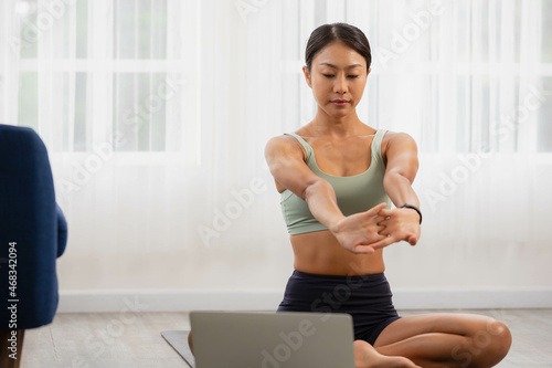 In the fitness studio, an Asian woman is studying online fitness training. Improve your health by extending meditating.