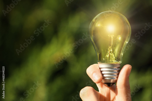 Woman holding glowing light bulb outdoors, closeup. Space for text