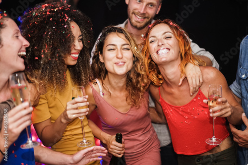Young multiracial friends dancing and drinking champagne at weekend party night - Focus on female faces