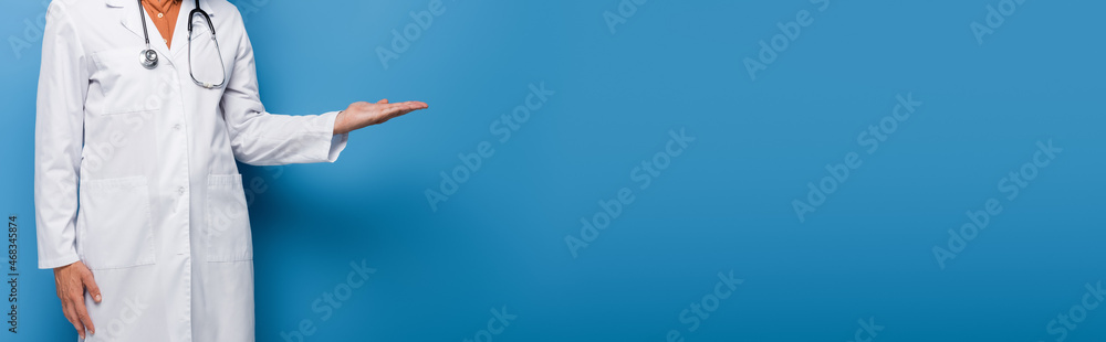 cropped view of doctor in white coat pointing with hand on blue, banner cropped view of doctor in white coat pointing with hand on blue, banner
