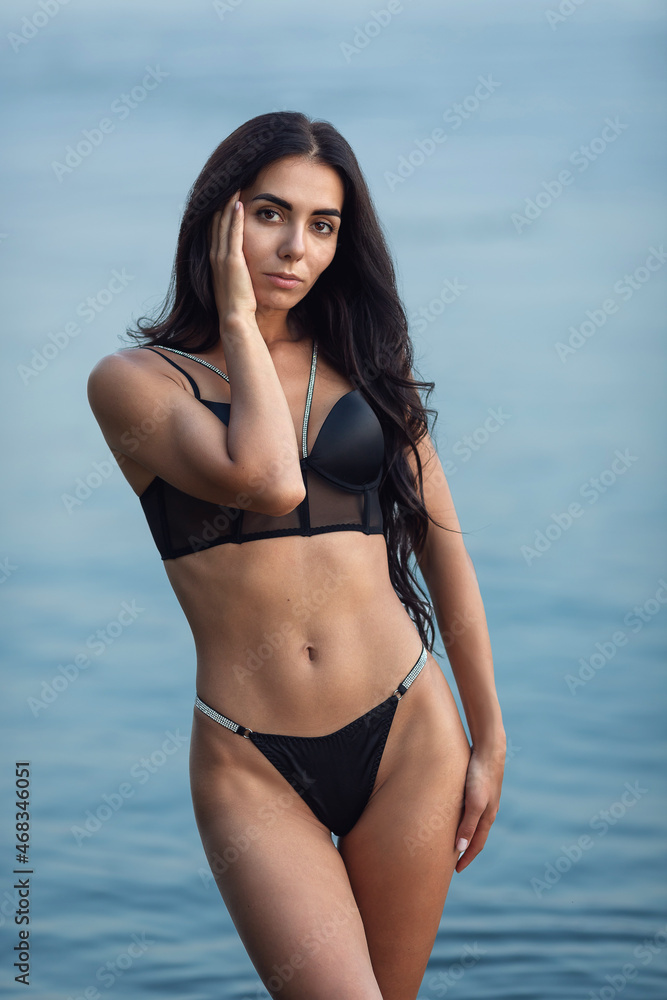 Young sexy brunette in a black bikini posing against the background of water. High quality photo Young sexy brunette in a black bikini posing against the background of water. High quality photo
