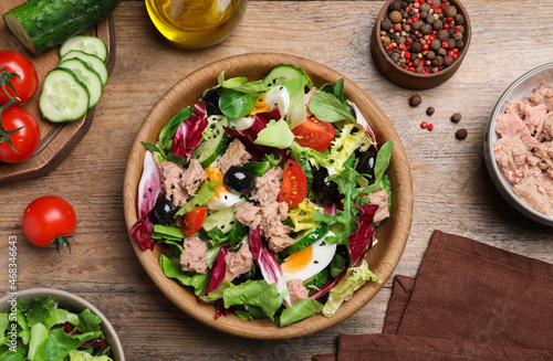 Bowl of delicious salad with canned tuna and ingredients on wooden table, flat lay