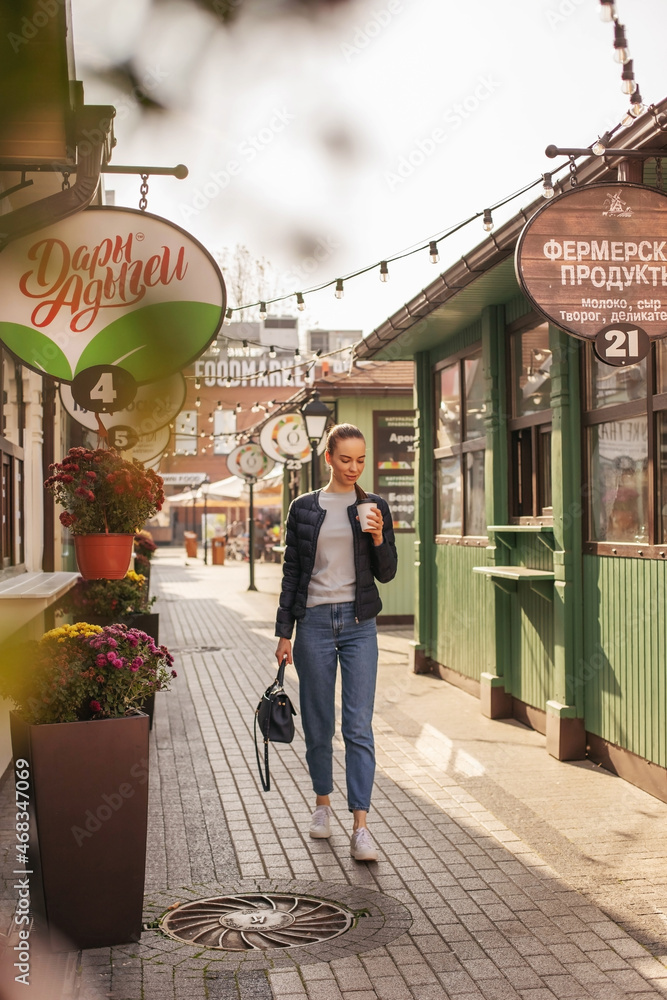 Obraz premium A girl walks through the central streets of the city drinking coffee.
