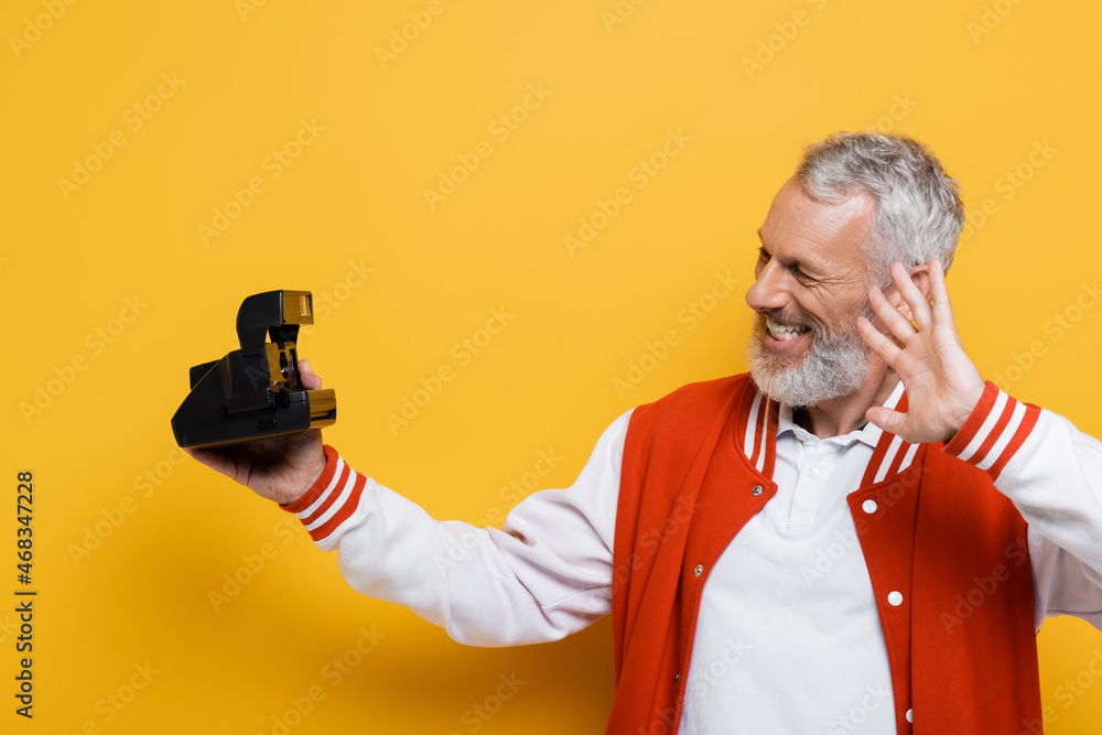 happy middle aged man in bomber jacket taking selfie on black vintage camera on yellow happy middle aged man in bomber jacket taking selfie on black vintage camera on yellow