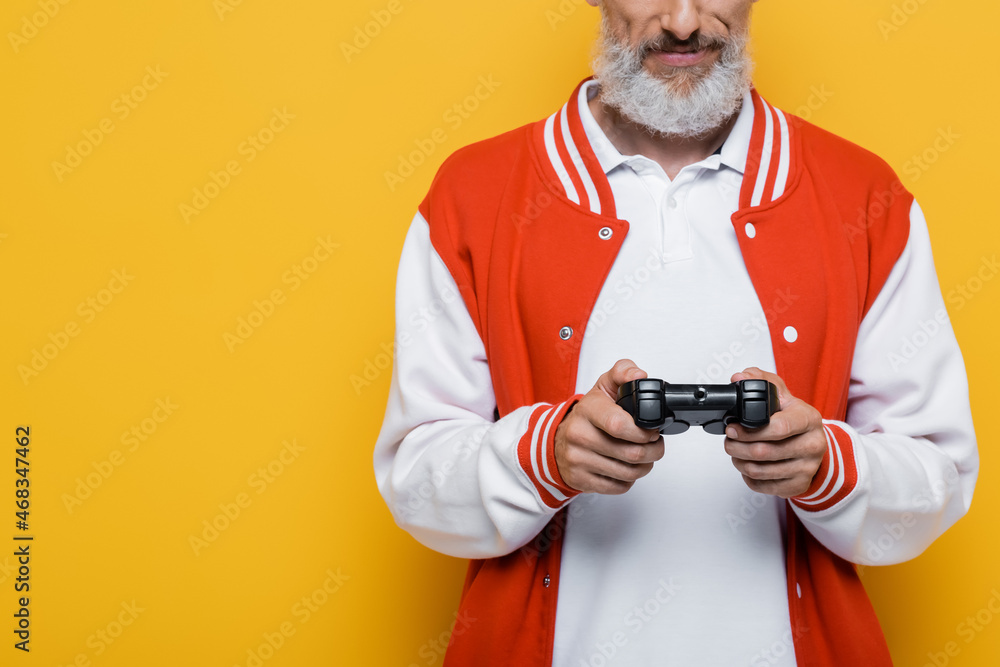KYIV, UKRAINE - JULY 29, 2021: cropped view of middle aged man in bomber jacket holding joystick on yellow KYIV, UKRAINE - JULY 29, 2021: cropped view of middle aged man in bomber jacket holding joystick on yellow